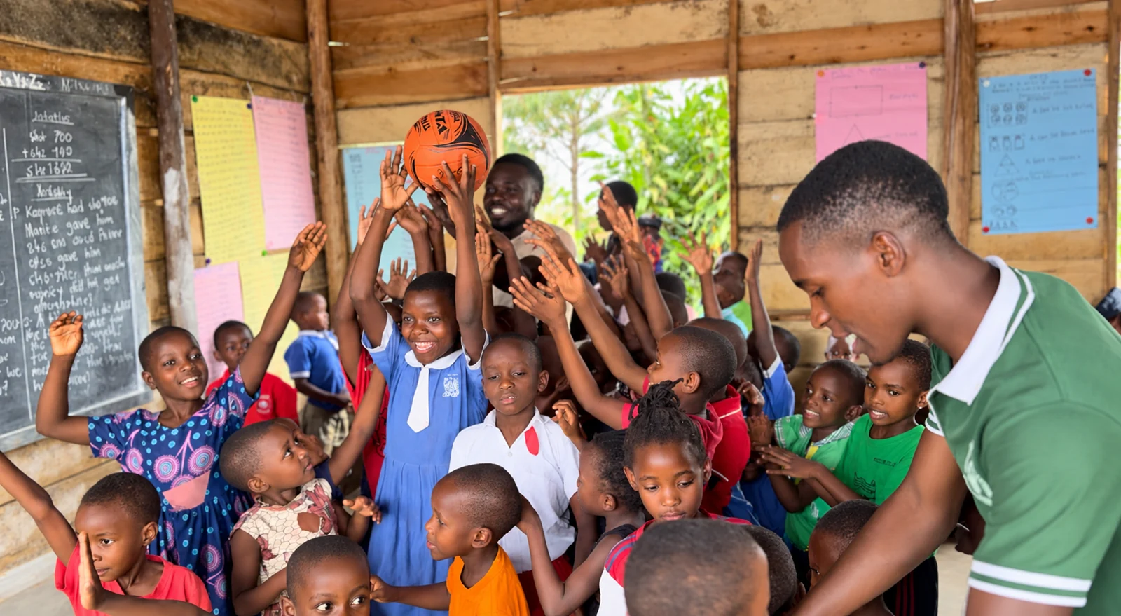 Children raising their hands around a ball during an activity in a classroom